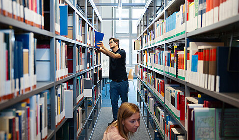 Eine Studentin und ein Student in der Bibliothek am Bücherregal © HTW Berlin