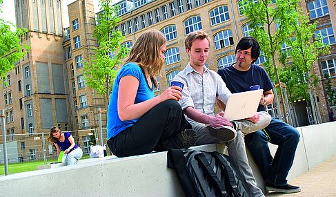 Drei Studierende sitzen am Campus Wilhelminenhof mit einem Kaffee to go im Freien  an einem Laptop © HTW Berlin