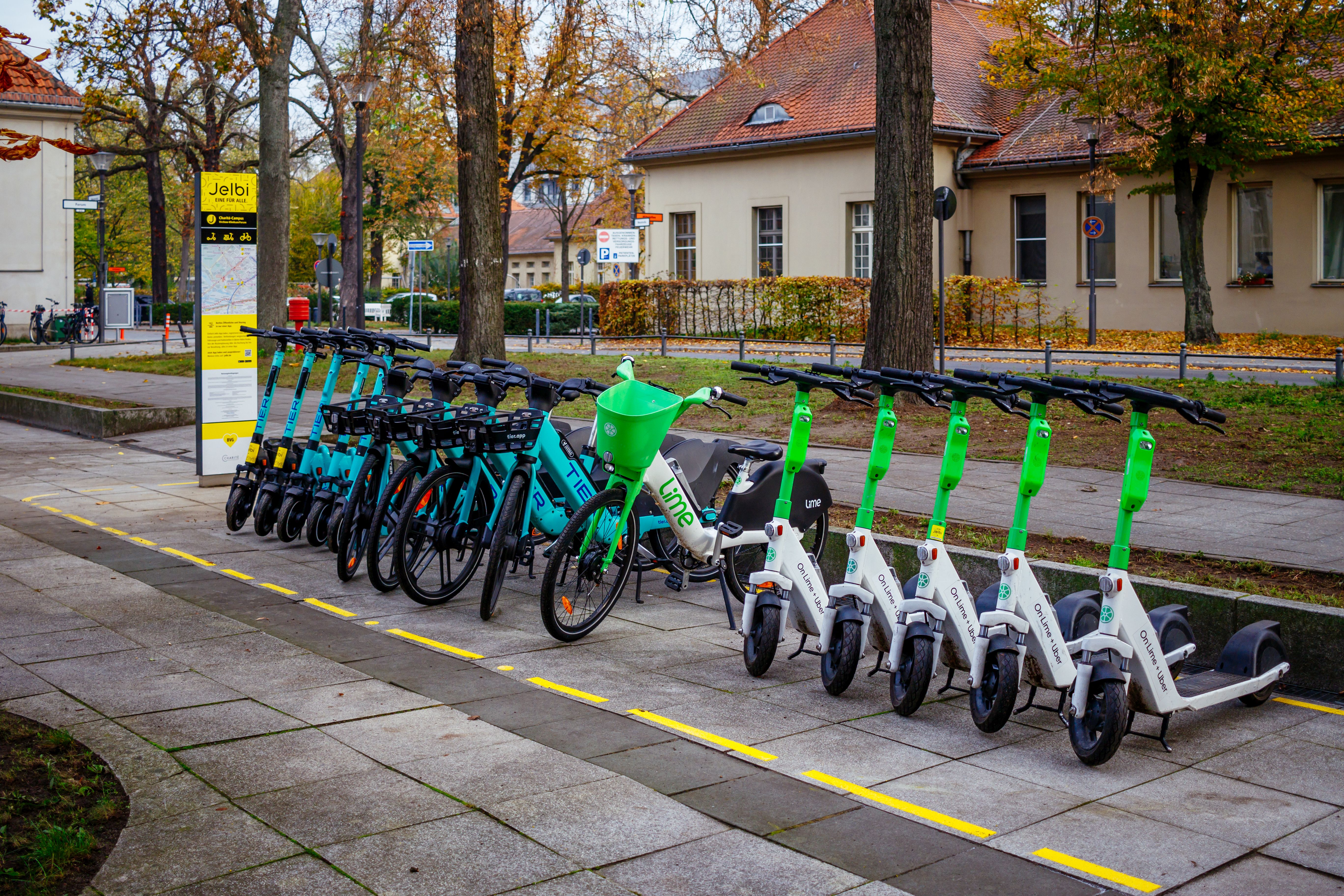 Foto eines Jelbi-Punkts in Berlin: Jelbi Schild, daneben Leihfahrräder und Scooter auf einer markierten Abstellfläche © BVG