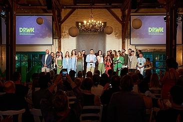 Ein Gruppe Menschen auf einer Bühne in einem festlichen Raum, im Hintergrund zwei Bildschirme mit dem Schriftzug "DPWK 2025" © DPWK